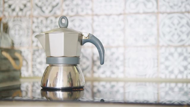  4K footage. Morning coffee preparation. Video of man's hands screwing up mokka coffee maker pot and putting it on modern glass kitchen stove top. Food preparation in modern kitchen concept