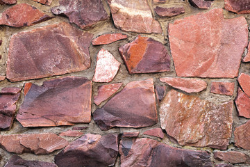 The wall of large raw granite stones of red color, background granite non-uniform