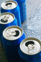Blue soda cans recycling closeup. Soda cans with open pull tab and condensation or water drops. Vertical image with selective focus.         