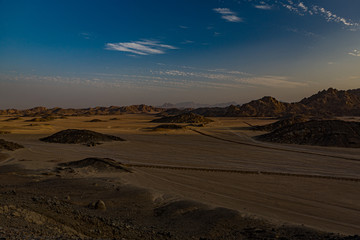 Safari and travel to Africa - extreme adventures or science expedition in a stone desert. Sahara desert at sunrise - mountain landscape with dust on skyline, hills and traces of the off-road car