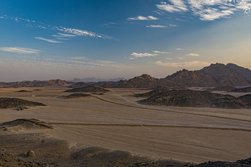 Safari and travel to Africa - extreme adventures or science expedition in a stone desert. Sahara desert at sunrise - mountain landscape with dust on skyline, hills and traces of the off-road car