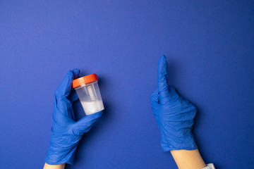 Female hands in latex blue gloves hold a plastic transparent container and point with their index finger upwards.