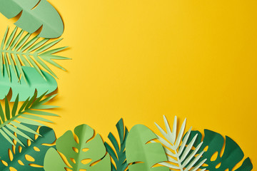 Fototapeta na wymiar top view of paper cut green palm leaves on yellow background with copy space