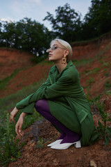Beautiful girl on the hill in a green jacket and sunglasses. Fashion portrait
