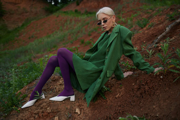 Beautiful girl on the hill in a green jacket and sunglasses. Fashion portrait