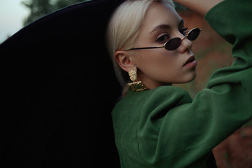 Beautiful girl on the hill in a green jacket and sunglasses. Fashion portrait