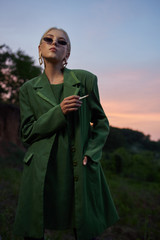 Beautiful girl on the hill in a green jacket and sunglasses. Fashion portrait
