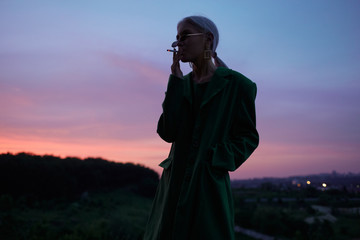 Beautiful girl on the hill in a green jacket and sunglasses. Fashion portrait