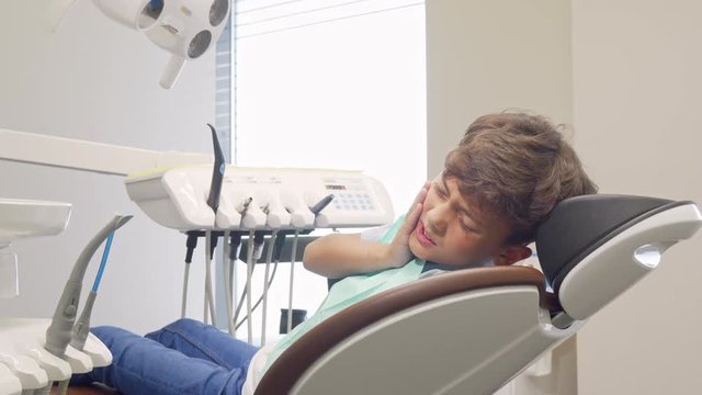 Little boy with toothache looking desperately to the camera. Young boy sitting in a dental chair, suffering from toothache. Child with unhealthy teeth at dentists office