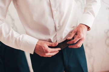Man's hands are worn on pants. Groom, stylish suit business. Wedding. Wear a belt. close up