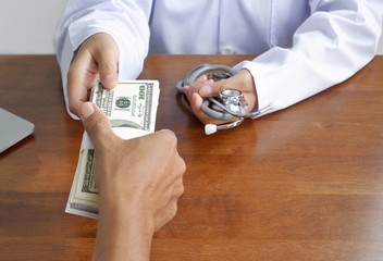 Selective focus of doctor's hand is recieving bundle of banknotes from anonymous hand at doctor...