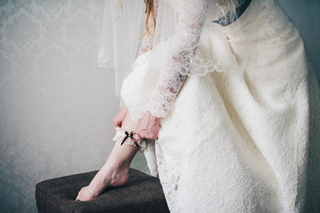 hand puts on a wedding garter armband on his leg. close-up. Morning Bride. wedding day. Stylish dress. mignonette. close up. part dresses. Against the background of white wall apartment.