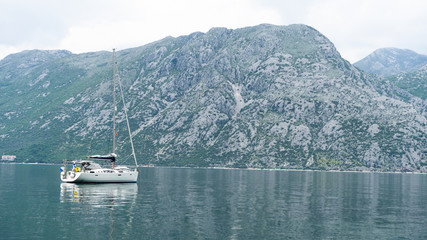 Fototapeta na wymiar Small Yacht in the Bay of Kotor in Montenegro. Marine boats. Relaxing landscape, boat in a calm sea. Grey mountain with green brushes