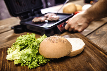 Cooking home burgers using electric grill on a wooden table