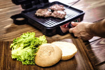 Cooking home burgers using electric grill on a wooden table