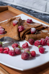  Pancakes on a white plate and a wooden tray with juicy berries, condensed milk and powdered sugar.
