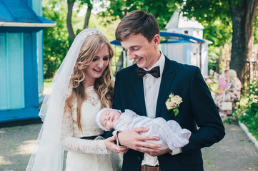 The bride and groom hold a small baby in their arms. Happy lovers on the wedding day. On the...
