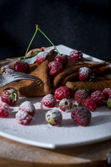  Pancakes on a black background with juicy berries, condensed milk and powdered sugar. Pancakes on a white plate and wooden oak board. Food on a black background. 
