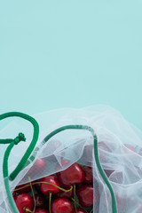 cherry in a reusable fabric transparent bag on a blue background in the fight against plastic. close-up space for text