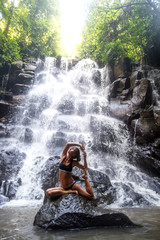 Woman practices yoga near waterfall in Bali, Indonesia