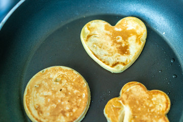 pancakes in the shape of a heart, flower and a circle on frying pan