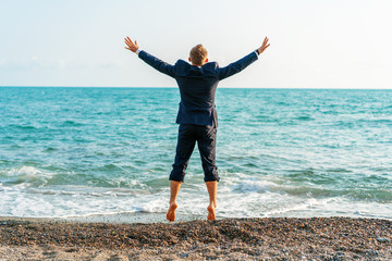 Happy businessman jumping on the beach. Man having fun by the sea. Summer vacation and travel concept