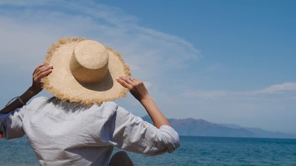 girl in shirt and hat sitting on the beach on a sunbed under an umbrella