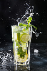 Splash of mojito cocktail or lemonade with lime and mint in glass on black. Close up. Summer drink.