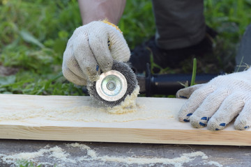 The carpenter is brushing a wood by a polishing disc for to create a textured surface on a wooden board.