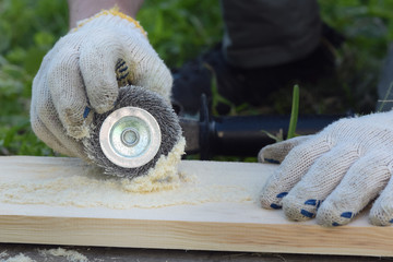 The carpenter is brushing a wood by a polishing disc for to create a textured surface on a wooden board.