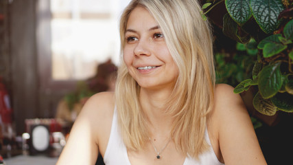 Portrait of smiling blonde sitting at coffee shop near green plants