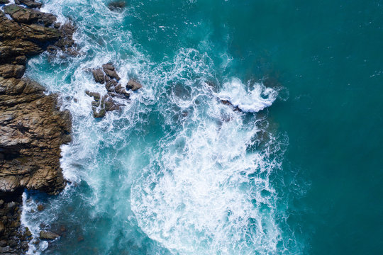 Aerial drone view of ocean's beautiful waves crashing on the rocky island coast