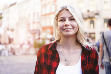 Lifestyle portrait of fashionable happy blonde girl wearing a rock red shirt, white t-shirt having fun outdoors in the city