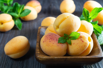 Fresh apricots in wooden bowl on dark wooden background.
