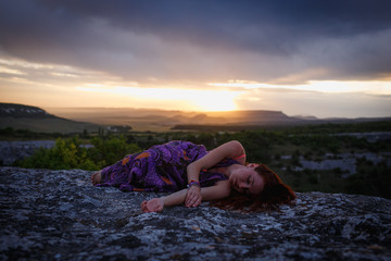 A woman lies on a rock and sleep while sun rising. Sunset on a mountain.