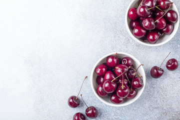 Fresh ripe red cherries in a white bowl on a gray stone background Copy space Top view