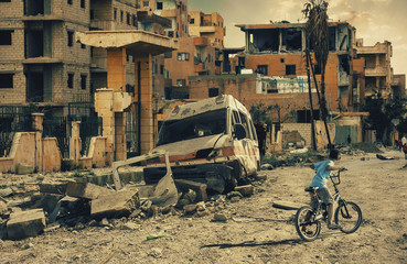 Homeless little boy riding bicycle in destroyed city, military soldiers and helicopters and tanks...