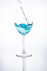 Blue cocktail is poured into a glass on a white background with reflection, splashes and bubbles