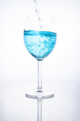 Blue cocktail is poured into a glass on a white background with reflection, splashes and bubbles