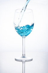 Blue cocktail is poured into a glass on a white background with reflection, splashes and bubbles