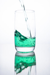 Green cocktail is poured into a glass on a white background with reflection, splashes and bubbles