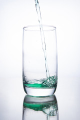 Green cocktail is poured into a glass on a white background with reflection, splashes and bubbles
