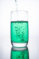 Green cocktail is poured into a glass on a white background with reflection, splashes and bubbles