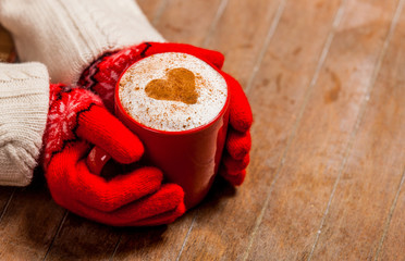 female hands in gloves holding cup of coffee on the wonderful brown wooden background