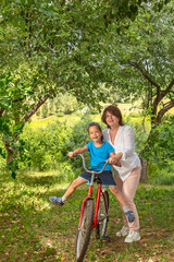 Fototapeta na wymiar A grandmother rides on a big red bike of a grandson in a garden or in a forest on a sunny summer day