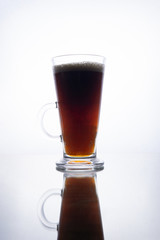 Dark beer in a mug on a white background with reflection