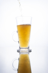 Light unfiltered beer poured into a steaming mug on a white background with reflection