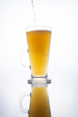 Light unfiltered beer poured into a steaming mug on a white background with reflection