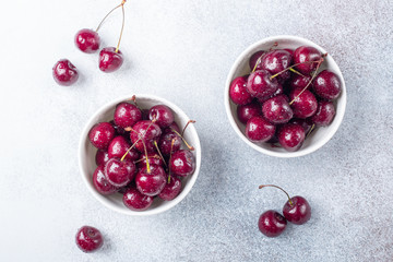 Fresh ripe red cherries in a white bowl on a gray stone background Closeup Water drops Top view