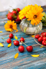 Summer on a wooden table: sweet cherry, green peas in the pods, strawberries, flowers